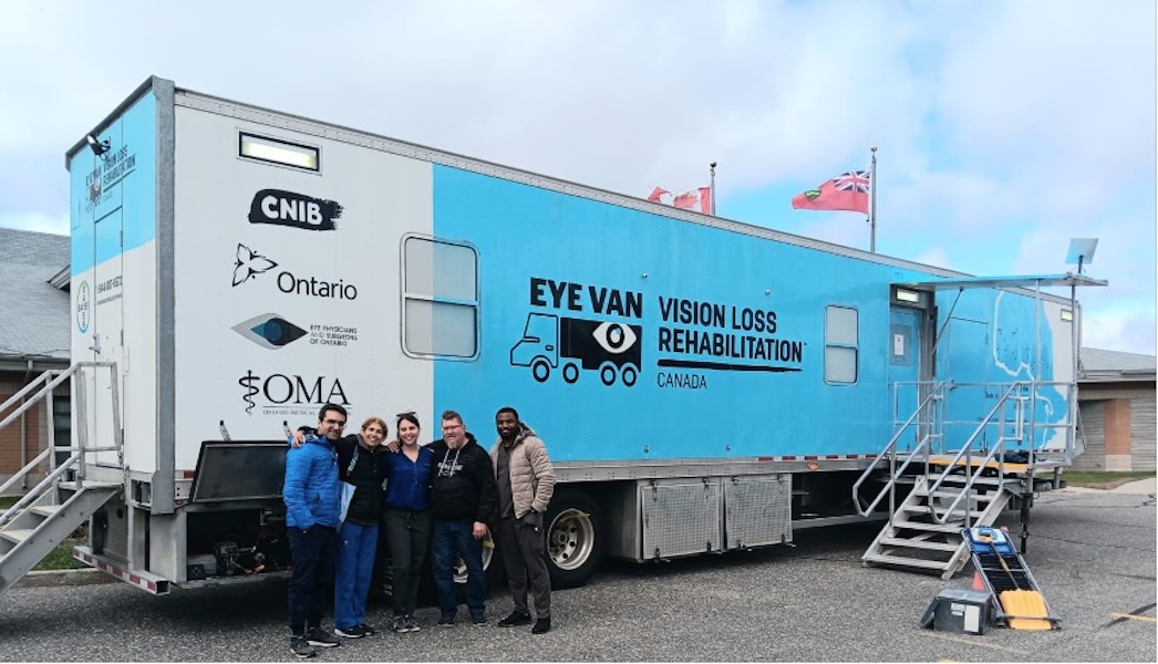 Photo of the blue VLRC Eye Van with the team standing before it