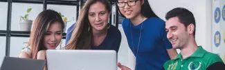 a group of 4 students looking at a laptop, smiling