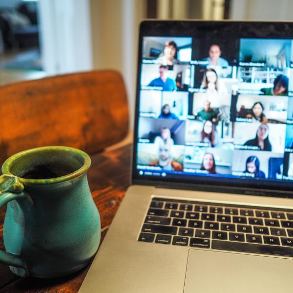 a mug and a laptop showing a large group on Zoom